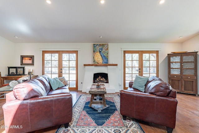 living room with recessed lighting, a warm lit fireplace, french doors, and light wood-style floors