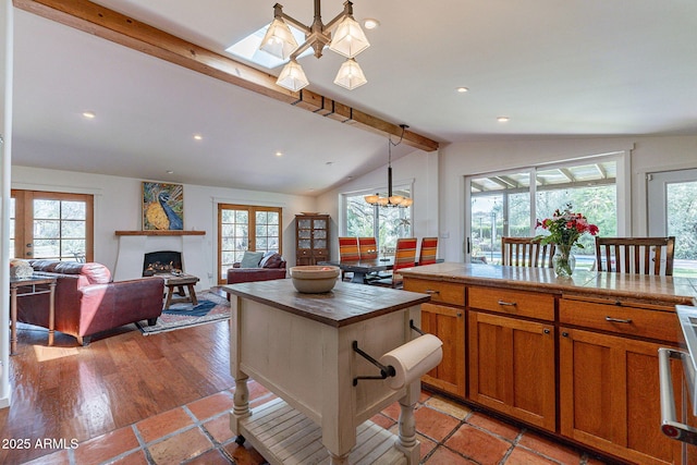 kitchen featuring plenty of natural light, vaulted ceiling with beams, brown cabinetry, and a fireplace