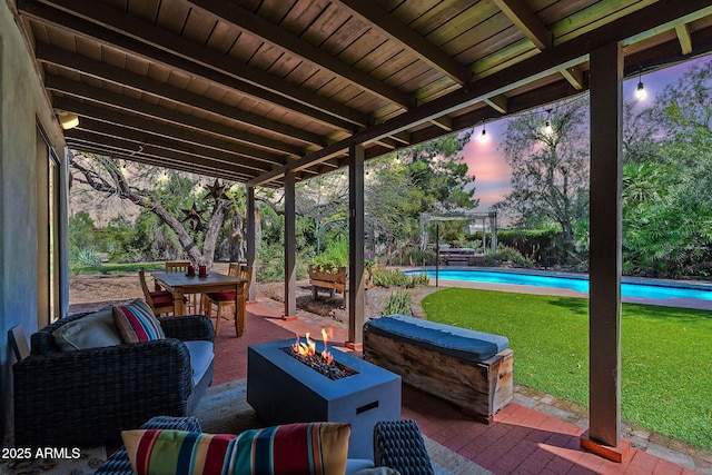 patio terrace at dusk featuring a lawn, outdoor dining space, a fire pit, and an outdoor pool