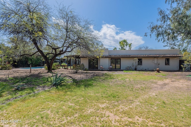 back of property featuring a lawn, an outdoor pool, stucco siding, and french doors