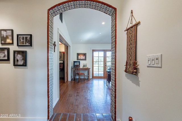 corridor featuring arched walkways, baseboards, and dark wood-type flooring