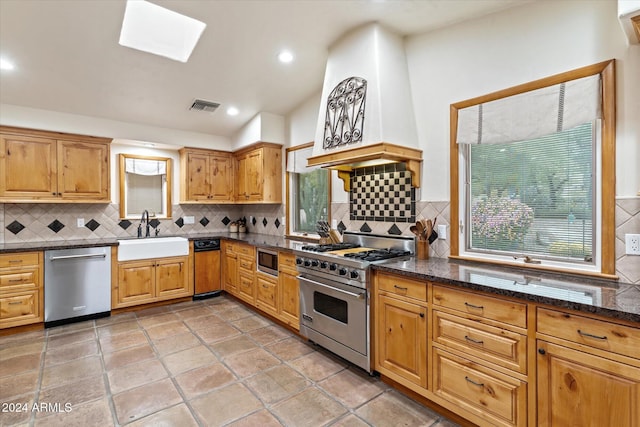 kitchen with a skylight, sink, dark stone countertops, decorative backsplash, and appliances with stainless steel finishes