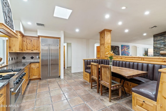 kitchen featuring decorative backsplash, a skylight, tile patterned floors, and high end appliances