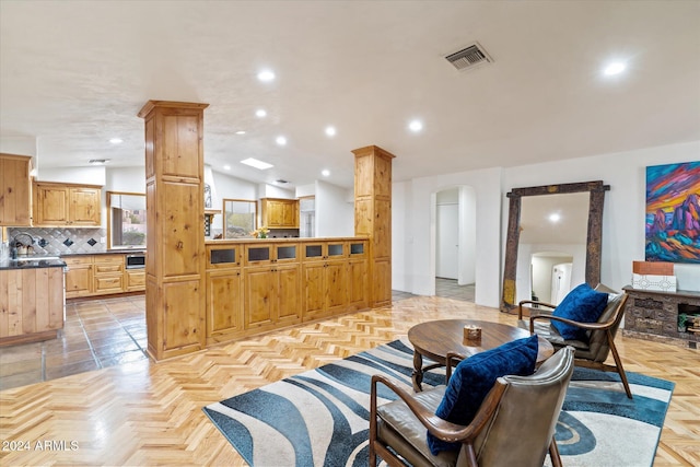 living room with decorative columns, light parquet floors, lofted ceiling, and sink