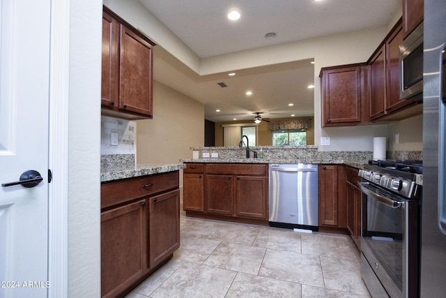 kitchen with kitchen peninsula, appliances with stainless steel finishes, light stone counters, ceiling fan, and sink