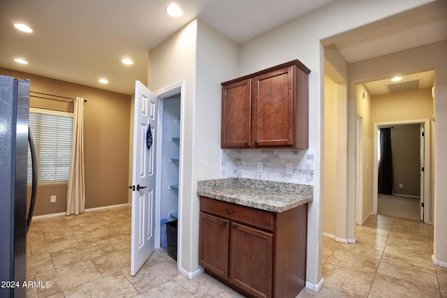 kitchen with decorative backsplash, stainless steel fridge, and light stone counters