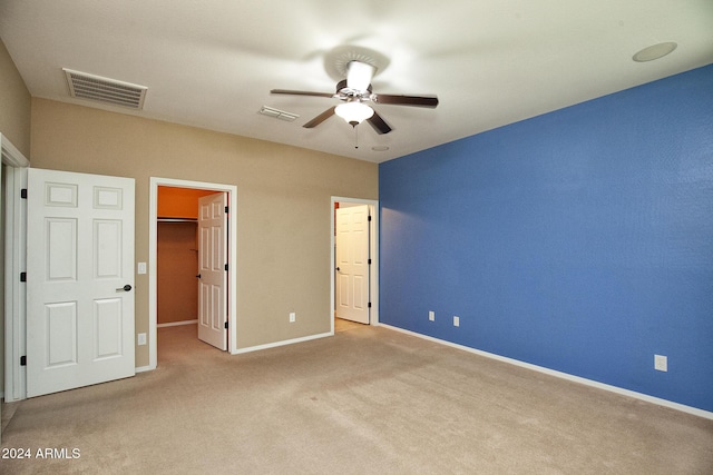 unfurnished bedroom featuring a walk in closet, ceiling fan, a closet, and light colored carpet