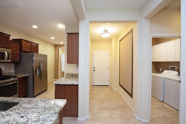 kitchen with dark brown cabinetry, stainless steel appliances, light stone counters, light tile patterned floors, and washer and dryer