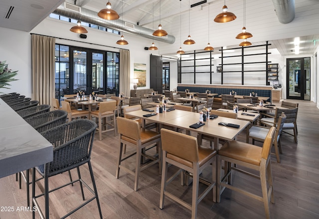 dining space featuring beamed ceiling, wood-type flooring, a towering ceiling, and french doors