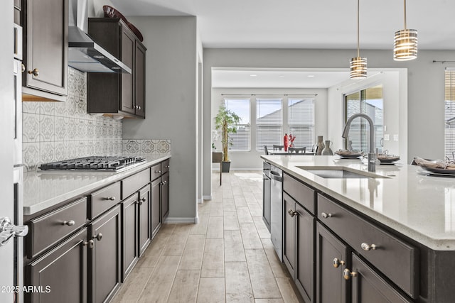 kitchen featuring appliances with stainless steel finishes, pendant lighting, sink, light stone counters, and wall chimney range hood