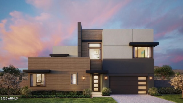 contemporary home with decorative driveway, a lawn, and an attached garage