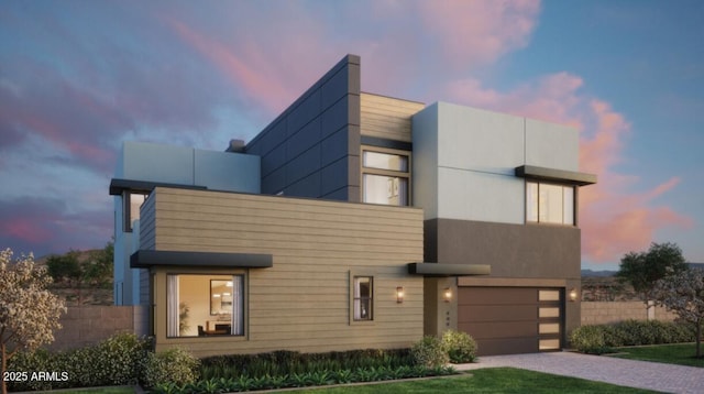 modern home with decorative driveway, fence, and stucco siding