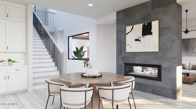 dining room with light wood-style floors, stairs, a tiled fireplace, and recessed lighting