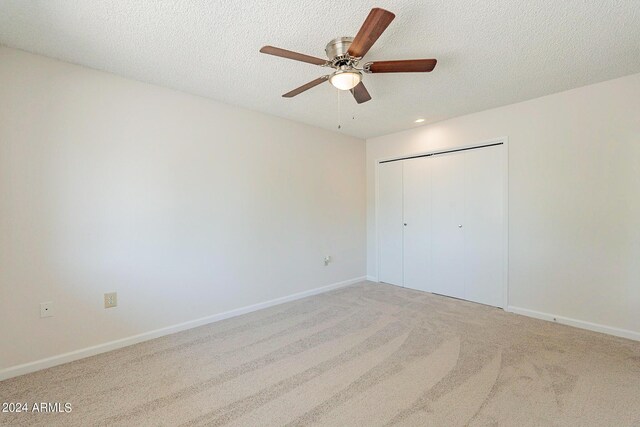 unfurnished bedroom featuring a textured ceiling, light colored carpet, a closet, and ceiling fan