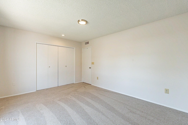 unfurnished bedroom featuring light carpet, a closet, and a textured ceiling