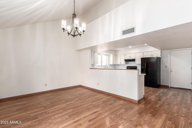 kitchen with a peninsula, visible vents, black fridge, under cabinet range hood, and wood finished floors