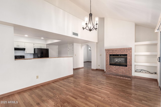 unfurnished living room with baseboards, a chandelier, a brick fireplace, visible vents, and wood finished floors