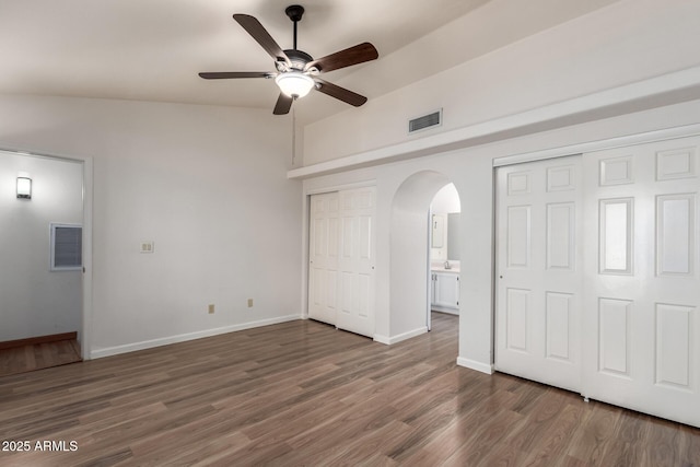unfurnished bedroom featuring visible vents, arched walkways, two closets, and wood finished floors