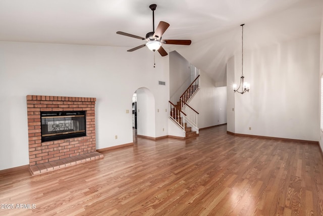 unfurnished living room featuring arched walkways, stairway, ceiling fan with notable chandelier, and wood finished floors