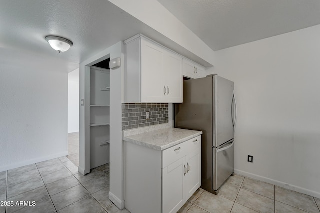 kitchen featuring light tile patterned flooring, stainless steel refrigerator, white cabinetry, backsplash, and a textured ceiling