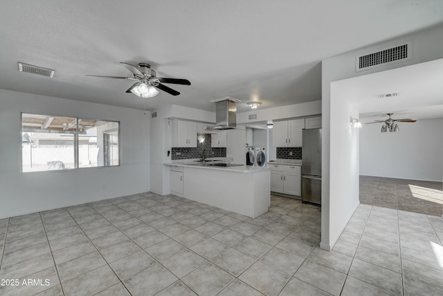 kitchen featuring stainless steel fridge, island range hood, washer and dryer, white cabinets, and kitchen peninsula