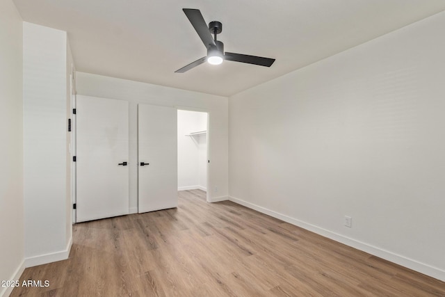 unfurnished bedroom with ceiling fan, a spacious closet, light wood-type flooring, and a closet