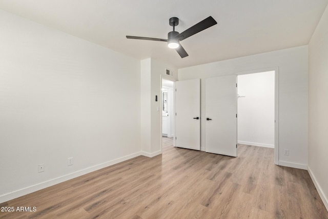 unfurnished bedroom featuring a closet, a walk in closet, ceiling fan, and light hardwood / wood-style flooring