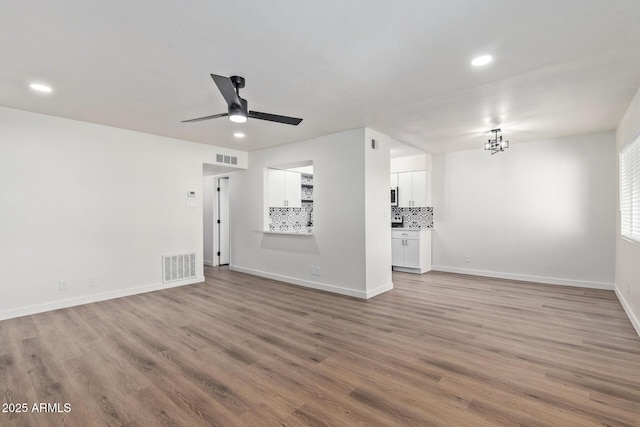 unfurnished living room featuring ceiling fan with notable chandelier and light hardwood / wood-style flooring