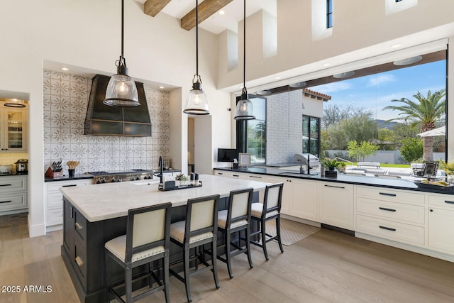 kitchen featuring a kitchen island with sink, hanging light fixtures, a kitchen breakfast bar, and premium range hood