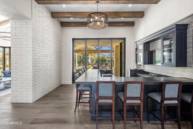 dining space featuring dark wood-type flooring, brick wall, sink, and beamed ceiling