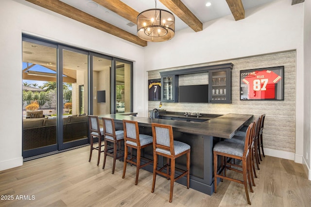 bar featuring beam ceiling, light hardwood / wood-style floors, hanging light fixtures, and a notable chandelier