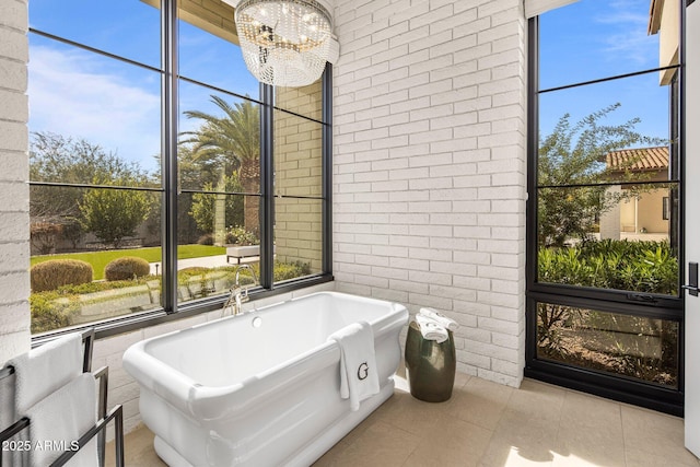 bathroom featuring tile patterned floors, a chandelier, a bathing tub, and brick wall