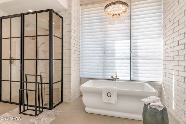 bathroom with tile patterned flooring, brick wall, a notable chandelier, and a tub to relax in