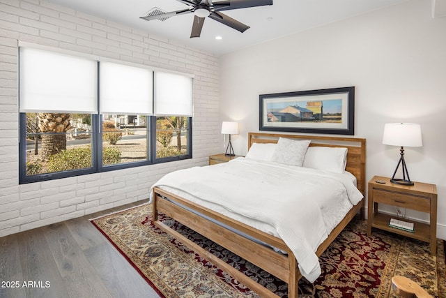 bedroom featuring dark hardwood / wood-style floors, ceiling fan, and brick wall