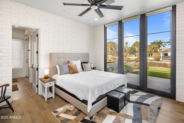 bedroom featuring multiple windows, light wood-type flooring, and brick wall