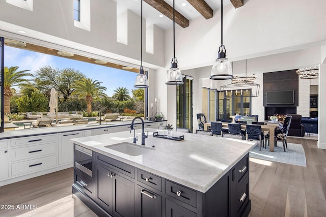 kitchen featuring sink, white cabinets, hanging light fixtures, a kitchen island with sink, and beam ceiling