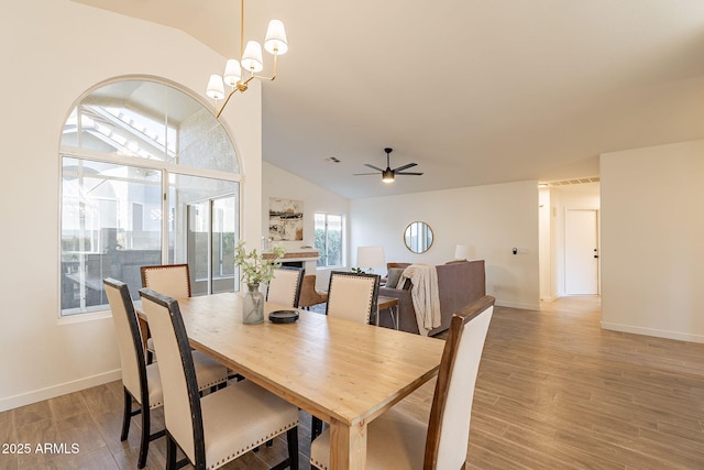 dining space with lofted ceiling, ceiling fan with notable chandelier, and light hardwood / wood-style flooring