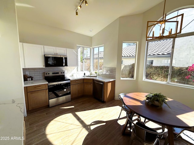 kitchen featuring stainless steel appliances, vaulted ceiling, white cabinets, and decorative backsplash