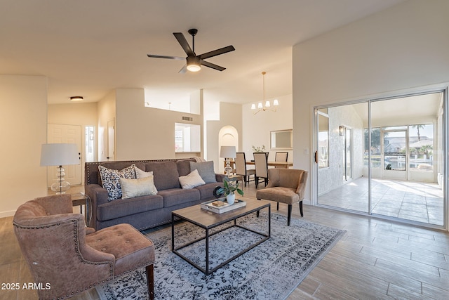 living room with ceiling fan with notable chandelier, wood-type flooring, and high vaulted ceiling