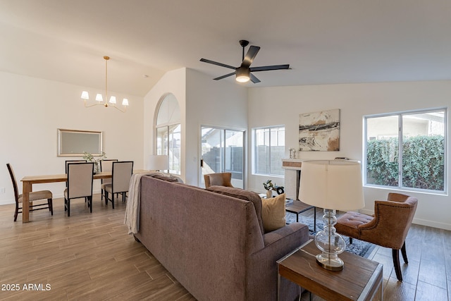 living room with plenty of natural light, ceiling fan with notable chandelier, lofted ceiling, and light wood-type flooring