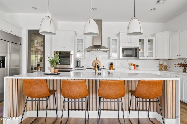 1500 E Sagittarius Pl, Chandler, AZ 85249 - kitchen featuring stainless steel appliances, wall chimney range hood, light countertops, a kitchen bar, and white cabinetry