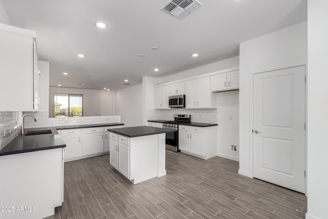 kitchen with stainless steel appliances, a sink, dark countertops, decorative backsplash, and white cabinetry