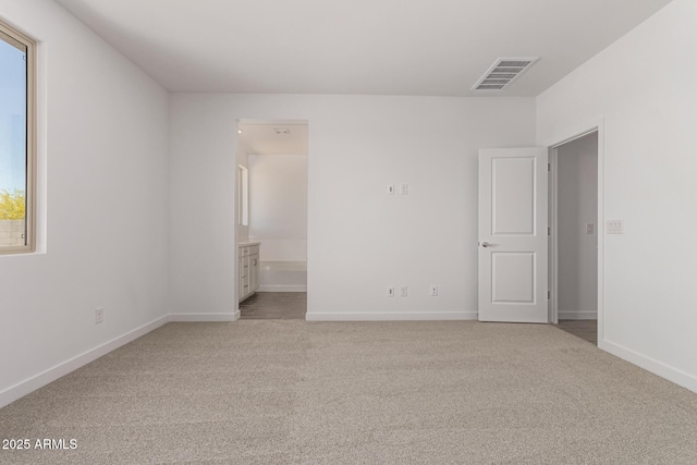 unfurnished bedroom featuring light colored carpet, baseboards, and ensuite bath