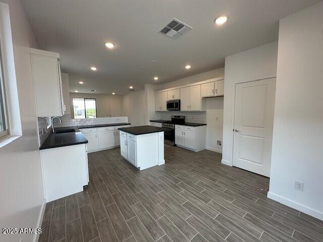 kitchen featuring appliances with stainless steel finishes, a sink, dark countertops, baseboards, and recessed lighting