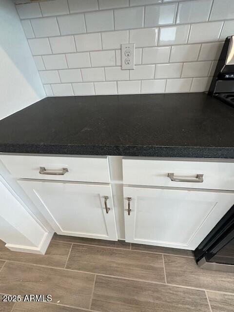 kitchen view of wood tiled floors, white cabinets, dark countertops, and decorative backsplash
