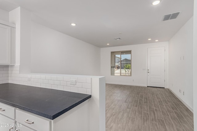 kitchen featuring white cabinetry, decorative backsplash, recessed lighting, dark countertops, and light wood finished floors