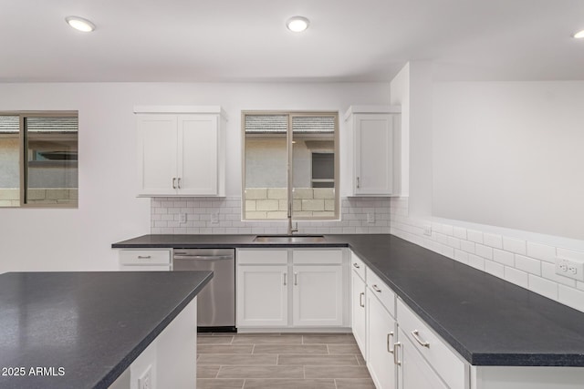 kitchen with stainless steel dishwasher, dark countertops, a sink, tasteful backsplash, and white cabinetry