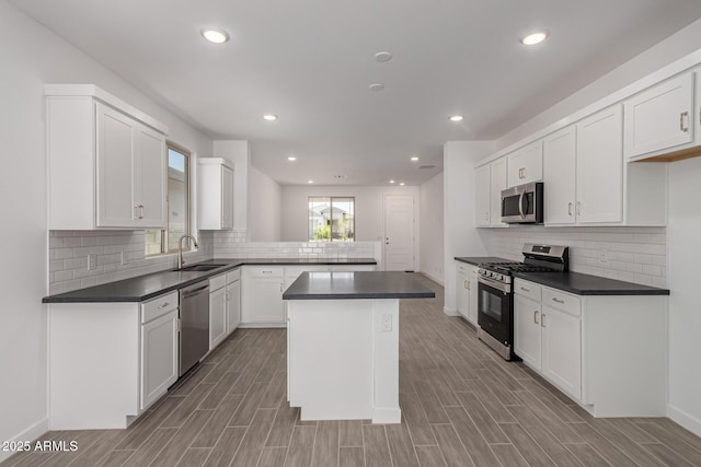 kitchen featuring stainless steel appliances, a sink, dark countertops, white cabinetry, and recessed lighting