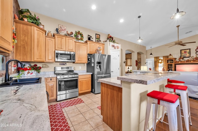 kitchen featuring sink, vaulted ceiling, appliances with stainless steel finishes, decorative light fixtures, and a breakfast bar area