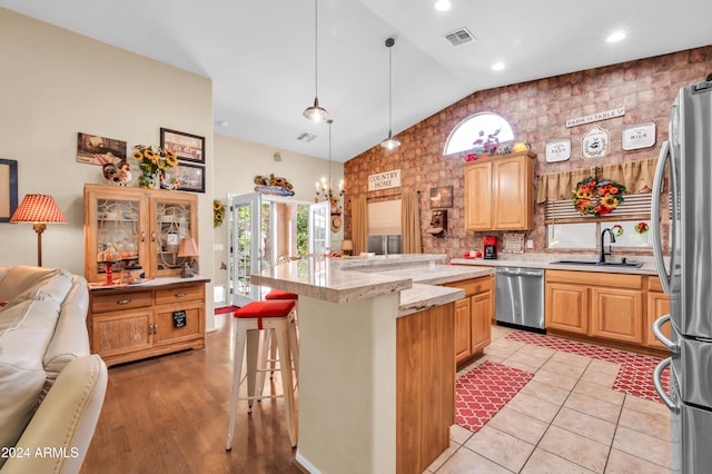 kitchen featuring a kitchen bar, appliances with stainless steel finishes, decorative light fixtures, a kitchen island, and lofted ceiling